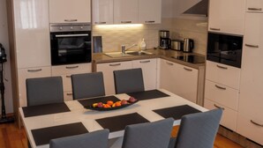Eine moderne Küche mit weißen Schränken, einem Backofen, einer Kaffeemaschine und einem Esstisch mit Stühlen.