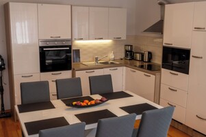 Una cocina moderna con armarios blancos, horno empotrado, cafetera y una mesa de comedor con sillas.