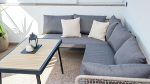 Ein sonnendurchfluteter Patio-Bereich mit einem grauen Sofa, einem kleinen Tisch und einem Korbstuhl.