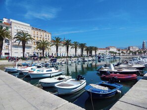 A marina with various boats docked, surrounded by buildings and palm trees. - Apartments Studio Spalato (Split)