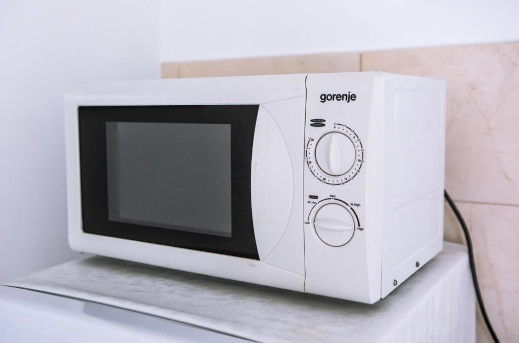 Een witte magnetron met het merk 'Gorenje' aan de rechterkant, op een wit oppervlak tegen een muur.