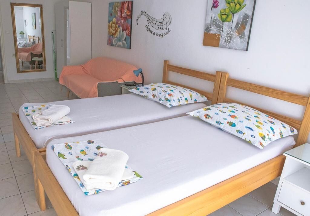 A double bed with white linens and colorful pillows, a wooden headboard, a bedside table, and a mirror.