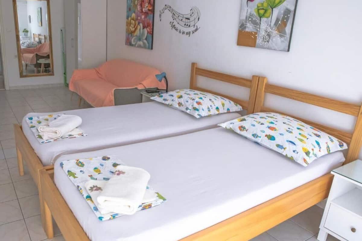 Una cama doble con ropa de cama blanca y almohadas coloridas, un cabecero de madera, una mesita de noche y un espejo.