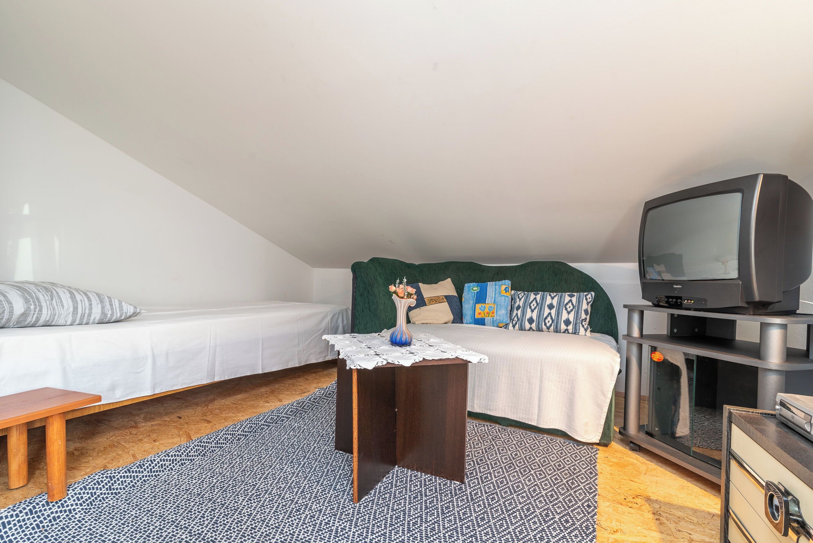 Ein Schlafzimmer mit einem Bett, einem kleinen Tisch mit Spitze, einem Fernseher auf einem Schrank und einer hölzernen Bank.