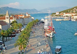 Eine Uferpromenade mit einem großen vor Anker liegenden Schiff, vorbei an einer von Palmen gesäumten Promenade, mit historischen Gebäuden im Hintergrund.
