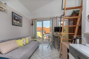 A compact living space with a sofa, a dining table, a kitchen area, and a sliding glass door leading to an outdoor patio. - Apartments Kate (Trogir)
