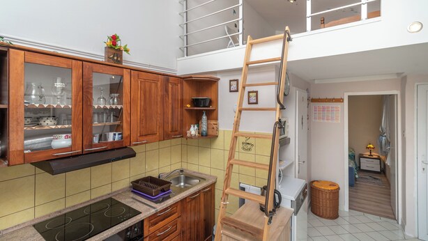 A kitchen with wooden cabinets, a built-in stove, and a loft bedroom with a ladder. - Apartments Kate (Trogir)