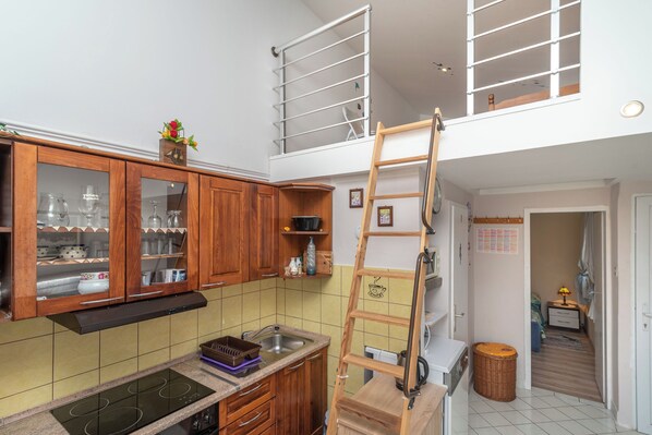 Eine Küche mit Holzausstattung, einem eingebauten Herd und einem Schlafzimmer auf Podest, erreichbar über eine Leiter.