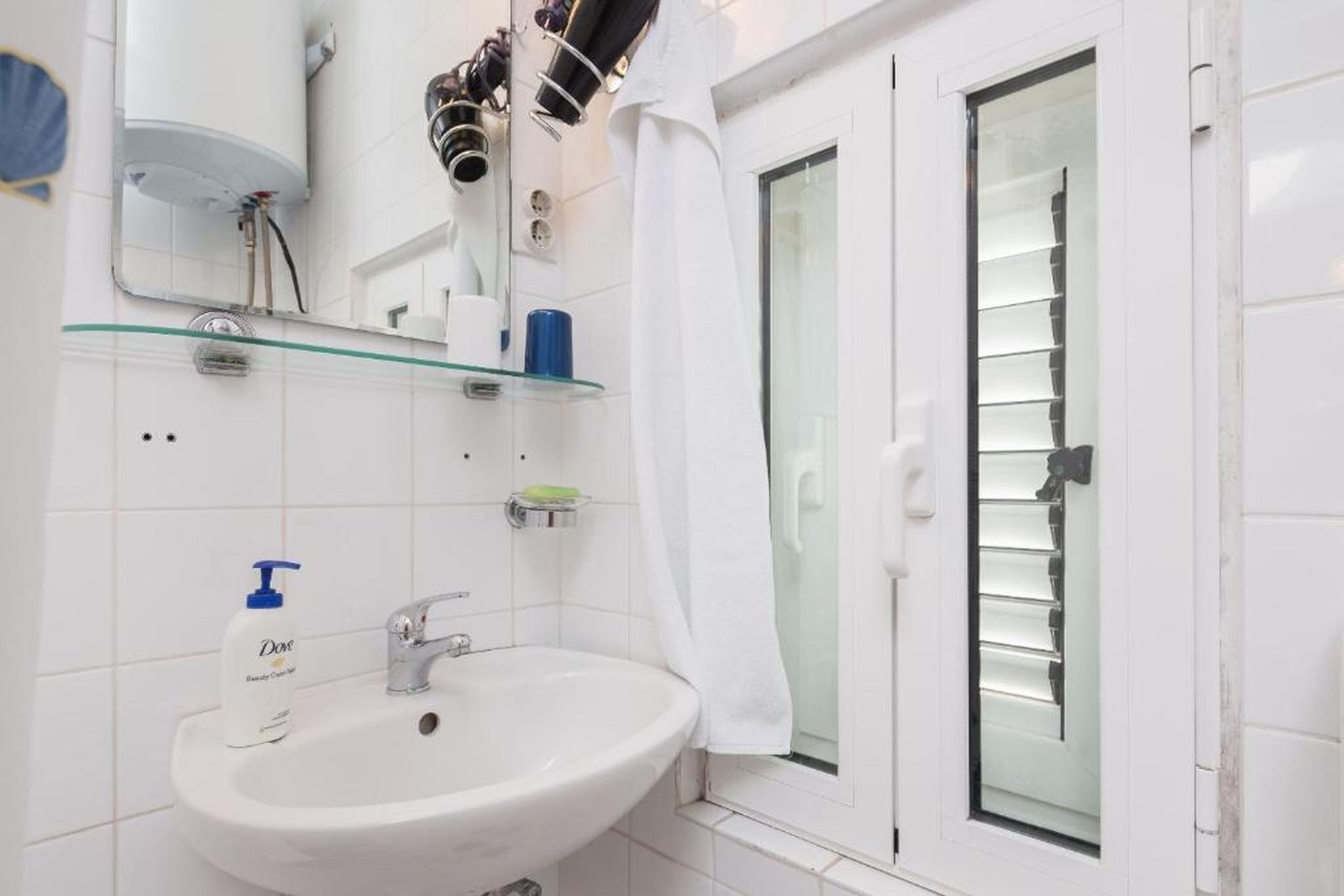 A bathroom with a white sink, a glass shelf, a mirror, and a shower with a glass door.