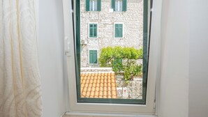 Ein Fenster mit Blick auf ein Steinhaus mit grünen Fensterläden, einem Ziegeldach und einem kleinen Baum.