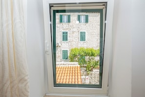 Ein Fenster mit Blick auf ein Steinhaus mit grünen Fensterläden, einem Ziegeldach und einem kleinen Baum.