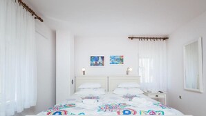 Ein weißes Himmelbett mit farbenfroher Bettdecke, zwei Wandlampen und zwei gerahmte Bilder an der Wand.