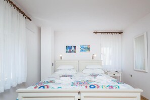 Ein weißes Himmelbett mit farbenfroher Bettdecke, zwei Wandlampen und zwei gerahmte Bilder an der Wand.