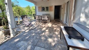 A covered outdoor area with a table and chairs, a ceiling fan, and a view of trees and buildings. - Apartment Sia (Crikvenica)