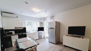A modern kitchen with a dining area, a refrigerator, a television, and a window providing natural light. - Apartment Sia (Crikvenica)