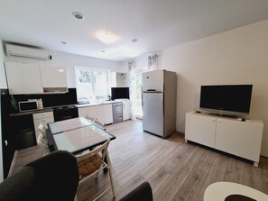 A modern kitchen with a dining area, a refrigerator, a television, and a window providing natural light. - Apartment Sia (Crikvenica)