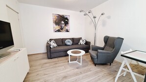 A modern living room with a sofa, armchair, coffee table, and a TV on a stand. - Apartment Sia (Crikvenica)