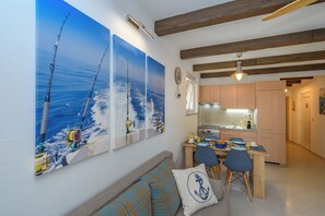 A modern kitchen with wooden beams, a dining area with a table and chairs, and a large painting of fishing scenes on the wall. - Apartment Kiara (Kraljevica)