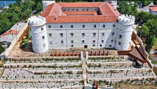 A large castle-like building with two prominent towers, a central courtyard with steps, and a red-tiled roof. - Apartment Kiara (Kraljevica)