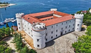 A castle with a red-tiled roof, two round towers, and a courtyard. - Apartment Kiara (Kraljevica)