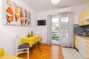A dining area with a yellow table, white chairs, a painting, a TV, and a kitchen with a view. - Apartments In Center (Jelsa)