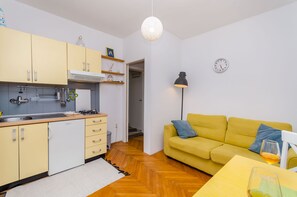 Ein kompakter Wohnbereich mit Küchenzeile, einem gelben Sofa, einem Esstisch und einer Lampe.