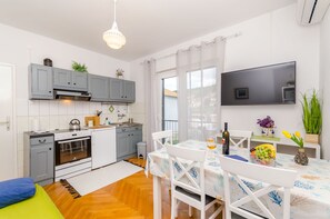 A modern kitchen with grey cabinets, a white stove, and a dining area with a table set for two. - Apartments In Center (Jelsa)