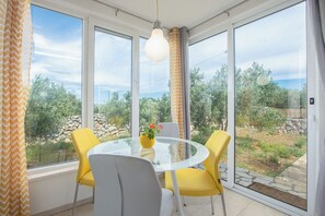 A room with a glass table, yellow chairs, a white chair, a hanging light fixture, and a view of greenery outside. - House Lila Jacuzzy (Trogir)