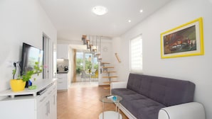 Ein modernes Wohnzimmer mit Sofa, Fernseher, Essbereich und einer Treppe.