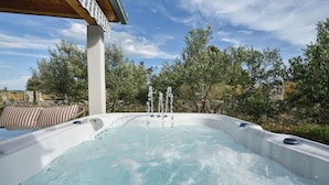 Ein Whirlpool mit zahlreichen Düsen, umgeben von Bäumen und einer Steinmauer.