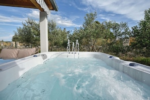 A hot tub with multiple jets, surrounded by trees and a stone wall. - House Lila Jacuzzy (Trogir)