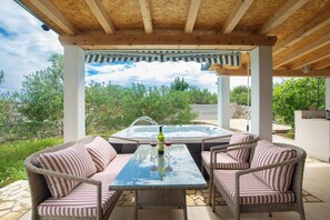 Eine Terrasse im Freien mit Korbmöbeln, einem Glastisch und einem Whirlpool.