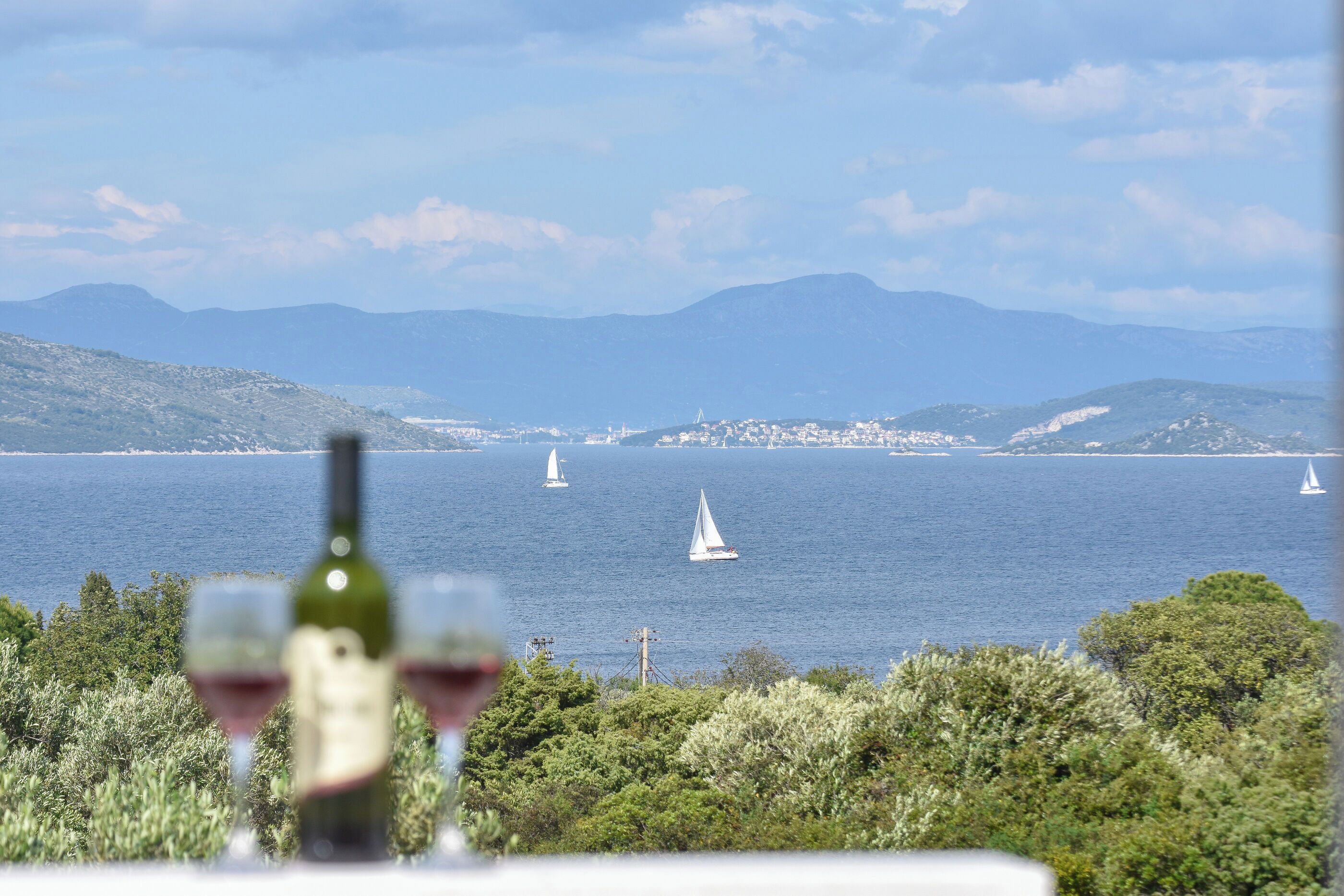 A coastal view with sailboats, a bottle of wine, and a table.