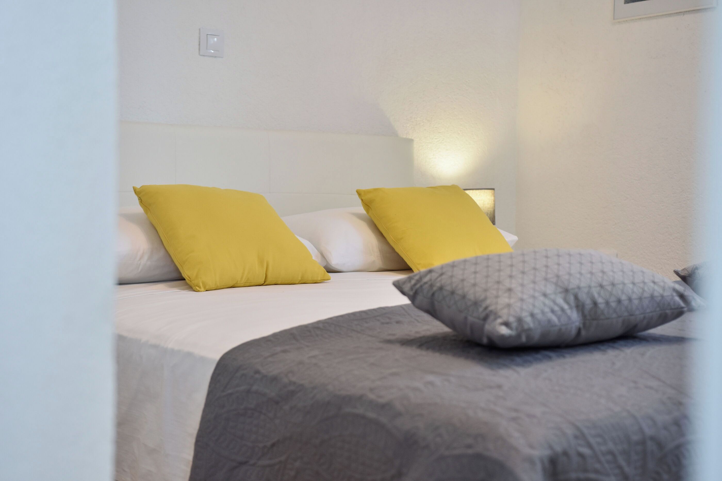 A bed with a white headboard, two yellow pillows, and a gray blanket.