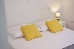 Ein Bett mit weißer Bettwäsche und zwei gelben Kissen, eine Nachttischlampe und eine weiße Wand.