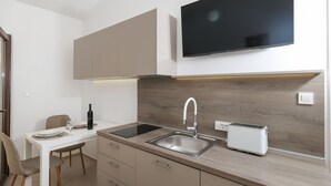 A modern kitchen with a flat-screen TV, a sink, a toaster, and a dining area with chairs and a table. - Apartments Andi (Sukosan)