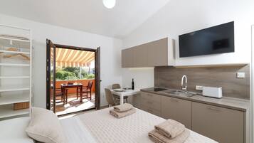 A modern hotel room with a bed, a TV, a kitchen area, and a balcony with a table and chairs.