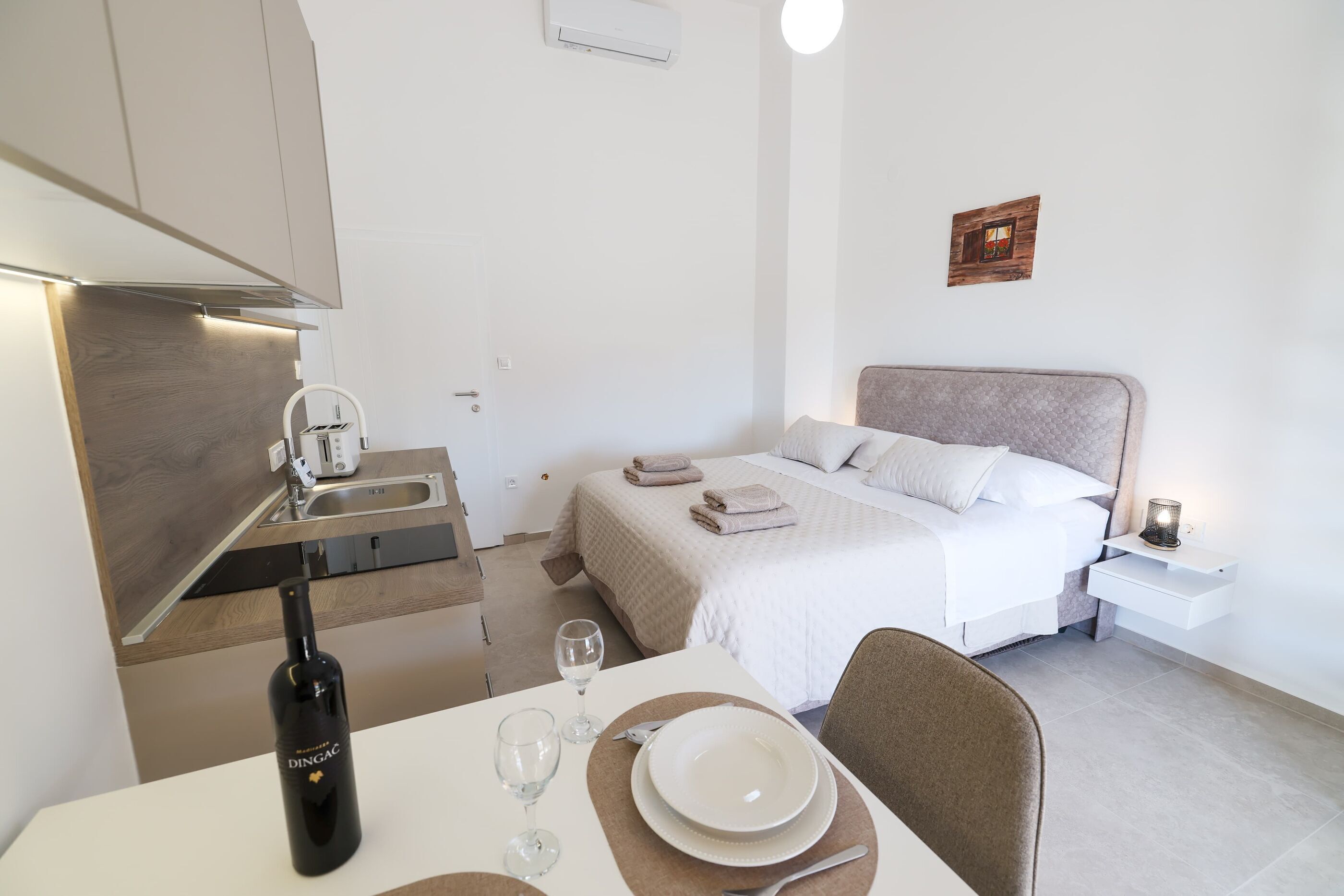 Ein modernes Hotelzimmer mit einem Bett, Nachttisch und einem Essbereich mit einer Weinflasche und Gläsern.