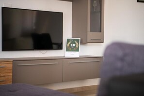 A hotel room with a large flat-screen TV mounted on the wall, a framed award certificate on the dresser, and a bed with a purple headboard. - House Ester (Liznjan)