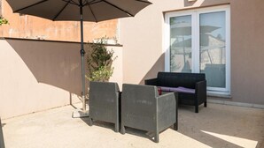An outdoor patio with two wicker chairs, a large umbrella, and a sliding glass door. - House Ester (Liznjan)