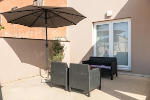 An outdoor patio with two wicker chairs, a large umbrella, and a sliding glass door. - House Ester (Liznjan)