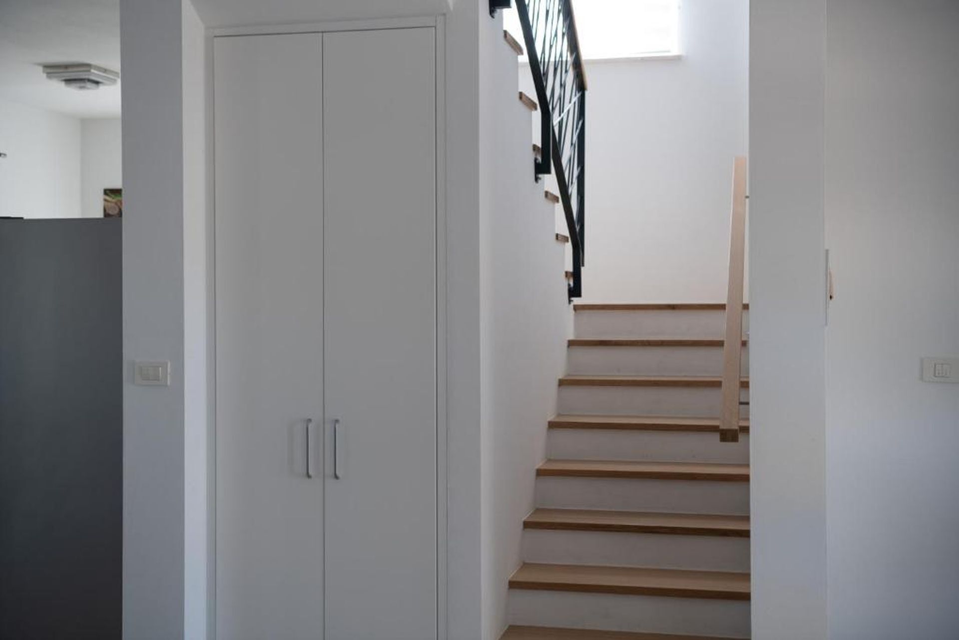 Una escalera de madera con barandilla negra, que conduce a un rellano con una puerta blanca.