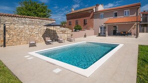 A swimming pool with lounge chairs, a stone wall, and a building with a tiled roof. - House Ester (Liznjan)