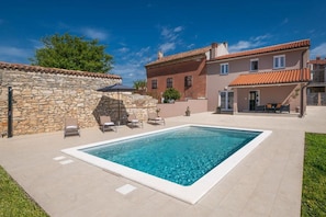 A swimming pool with lounge chairs, a stone wall, and a building with a tiled roof. - House Ester (Liznjan)