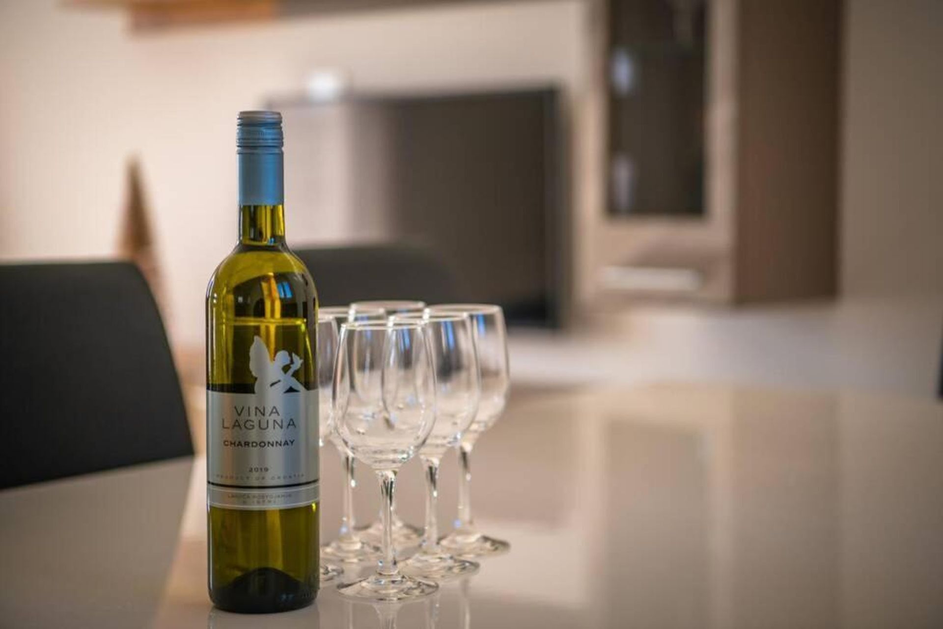 Una bottiglia di Vina Laguna Chardonnay su un tavolo con diversi bicchieri da vino vuoti.