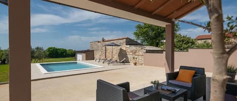 A covered outdoor area with a swimming pool, stone building, and outdoor furniture.