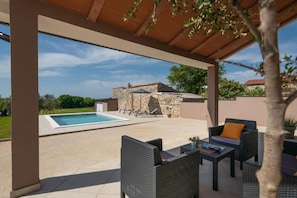 A covered outdoor area with a swimming pool, stone building, and outdoor furniture. - House Ester (Liznjan)