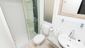 A bathroom with a glass shower enclosure, a toilet, a sink with a mirror, and a glass shelf. - Mobile Home Fisherman (Pasman)