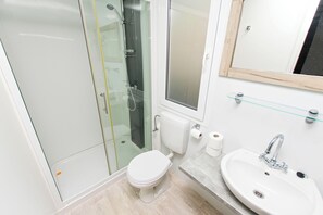 Ein Badezimmer mit Duschkabine aus Glas, Toilette, Waschbecken mit Spiegel und einer Glasablage.