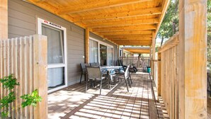 A covered outdoor area with a wooden deck, a table with chairs, and a window with a sign. - Mobile Home Fisherman (Pasman)